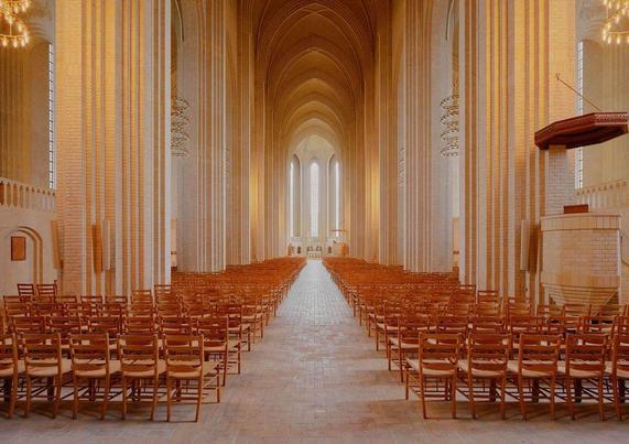A spacious church interior featuring rows of wooden chairs, high arched ceilings, and large windows allowing natural light.