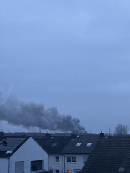 Foto aus einem Dachfenster. Man sieht weit hinten eine dicke und dunkle Rauchwolke