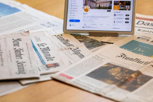 Zeitungen vor einem Bildschirm mit den Social-Media-Kanälen des DHIP