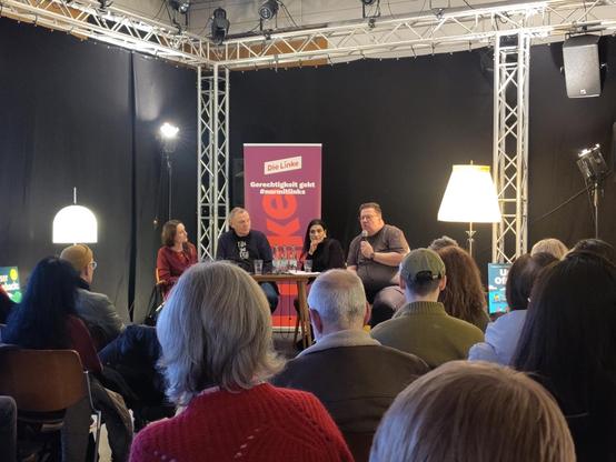 Blick über die Teilnehmenden auf das Podium mit Gizem Erinc-Cifci, Jan van Aken und Markus Philippi