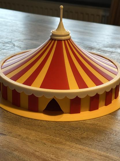 Großes 3D gedrucktes Zirkuszelt. Gelb rot gestreift mit weißer Porte und weißem Mast.
