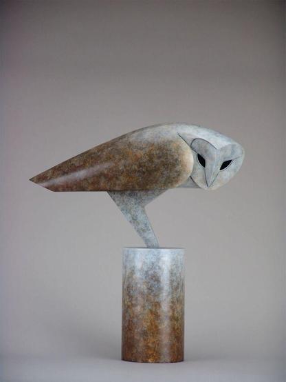 Stylized sculpture of an owl perched on a cylindrical base, featuring textured, earthy tones and striking black eyes.