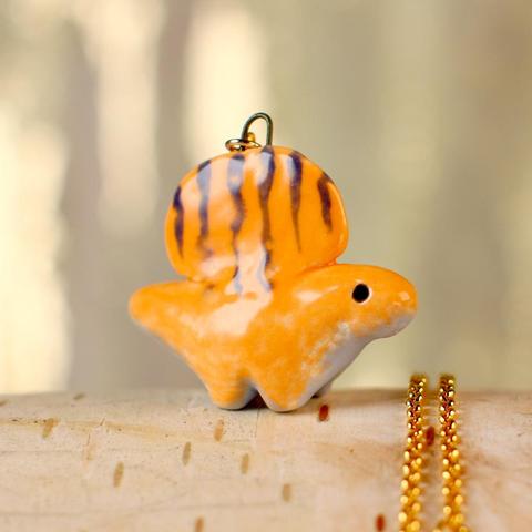 An orange ceramic dimetrodon pendant with navy stripes and a periwinkle belly on a gold-plated chain.