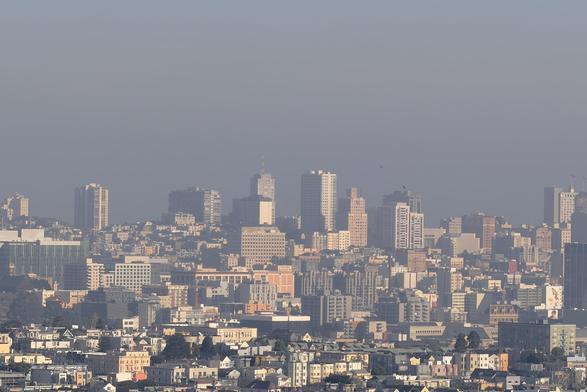 A view of a section of small high-rise buildings and lots of other urban small buildings in a very hazy conditions. The air pollution makes the light on the buildings reddish, and any background or landscape behind the buildings is completely obscured by the thick beige and gray wall of smoggy haze. 

A very air-polluted slice of San Francisco.