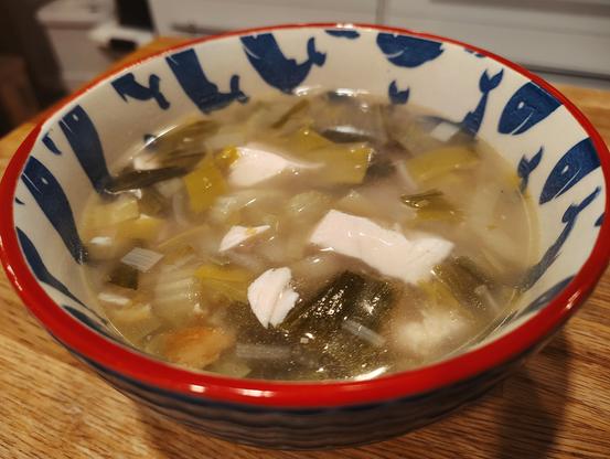 A bowl of soup with chunks of chicken, celery and leek visible.