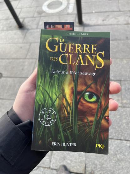 a book titled "La Guerre des Clans: Retour à l'état sauvage" by Erin Hunter. The cover features a cat's eye peering through grass