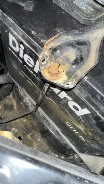Close-up of the battery hold-down bracket and rusted stud on a DieHard battery inside a Toyota FJ Cruiser engine bay.