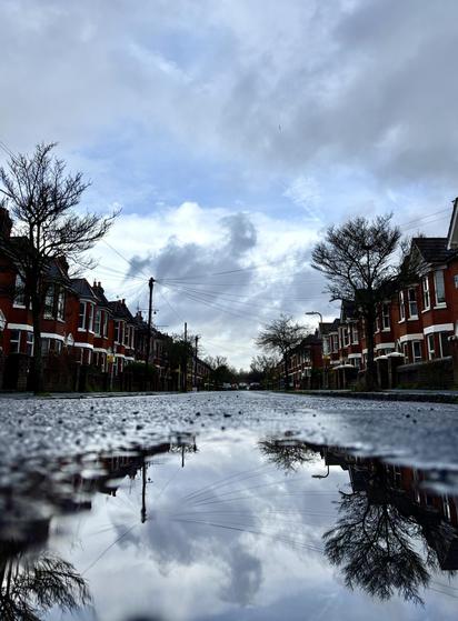 The same street as reflected in a puddle in the middle of the road.