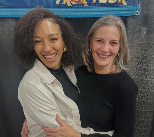 Tawny Newsome and Terry Farrell are smiling and embracing at a Star Trek convention.