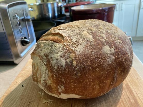 A very dark brown loaf of sourdough bread, dusted lightly with flour on top. it snaps and crackles loudly as it cools