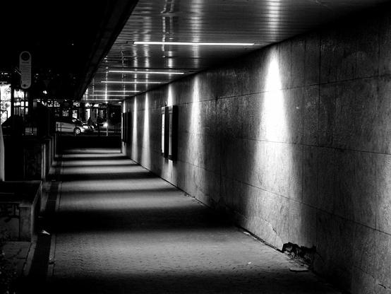 Eine überdachte Passage die durch die Beleuchtung mit langen Schatten horizontal und vertikal unterteilt ist.