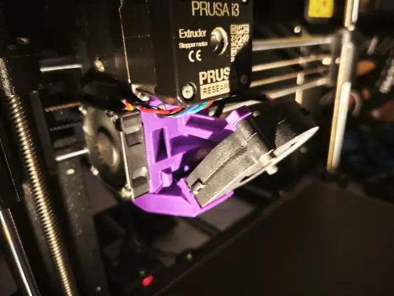 It's dark. 
A flashlight brightens a 3f printer. 
There are new parts for the fan shroud assembly in purple. 
you can see a bit of the extruder and a attached fan.