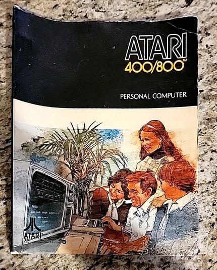 cover of booklet: ATARI 400/800 PERSONAL COMPUTER

illustrated by an image of family and indoor plant cheerfully huddled at the computer and its cassette deck for loading programs