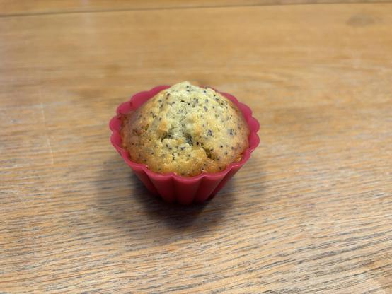 Ein Muffin in einer rosa Silikon-Muffinform auf einer Holztischplatte. Der Teig ist hell und enthält kleine schwarze Pünktchen.