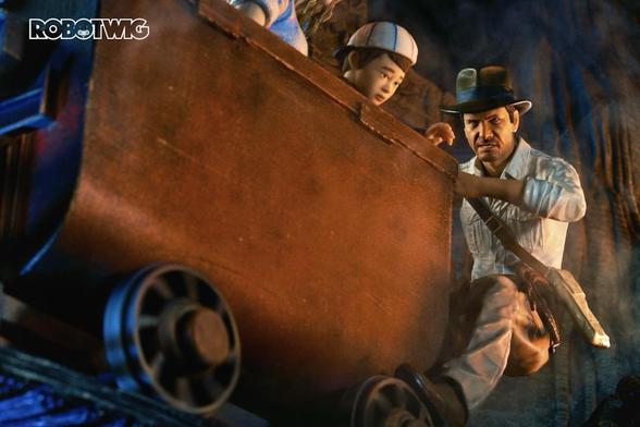 Indiana Jones tries to stop a runaway minecart with his foot on the wheel. Short Round watches from inside the cart