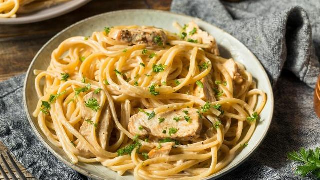 Un plato de espagueti Alfredo con pollo, decorado con perejil fresco.