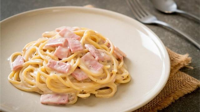 Un plato de espagueti con jamón y nata.