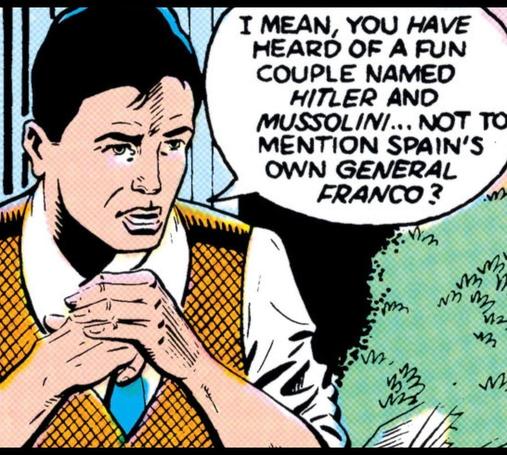 A man sets at a table outside as if on the patio of a restaurant. His elbows are on the table. He lays one hand on top of the other as he looks off to the right at somebody and says, “I mean you HAVE heard of a fun couple named HITLER and MUSSOLINI… Not to mention Spain’s own GENERAL FRANCO?“