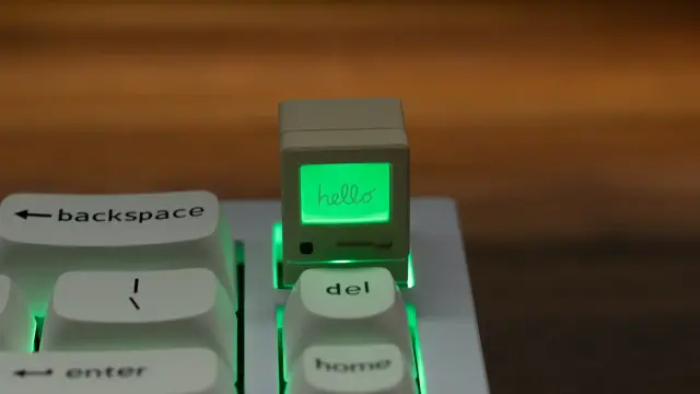 A keycap that is a replica of the original 1984 Macintosh standing tall on a keyboard
