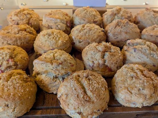 Colour photograph of a wooden board containing a large number of golden Brown scones topped with a crumble mix.