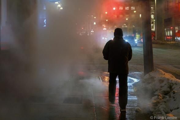 a figure walks past a steam vent on a cold night