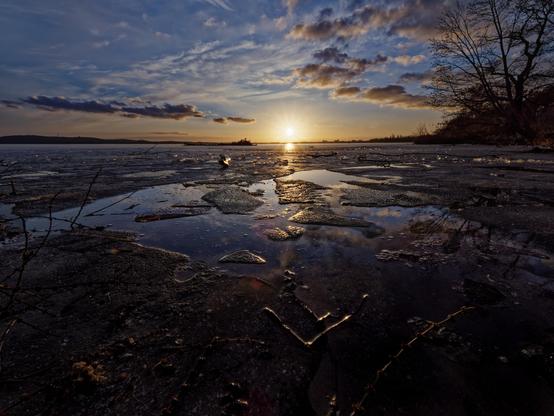 Sonnenuntergang über dem Müggelsee auf dem Wasser Eisschollen. Wolken am Himmel, die sich in den Pfützen spiegeln.