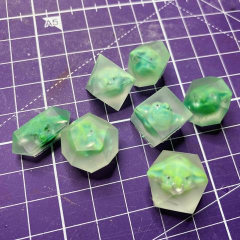 Seven polyhedral shapes, each with one of the green goblin heads from the previous post inside. The shapes are clear resin but because the surfaces aren't polished, they look like frosted glass, so you can see inside but not clearly. 

The heads now have silver jewelry, some moss hair and some velvet flock stubble. The shapes have some green iridescent flakes behind the goblin heads, also very hard to see. But after the final casting, all will be visible!