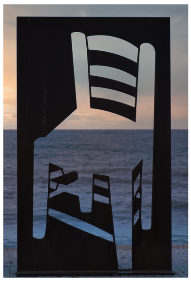 Kunst im öffentlichen Raum am Strand von Altea, eine Metallskulptur zeigt Negativformen des 'Stuhl in Arles mit Pfeife 1888' als Hommage an den Maler Van Gogh. Dahinter dunkles Meer und Abendhimmel.