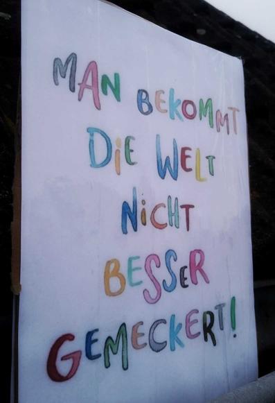 Demo-Plakat in bunter Schrift: man bekommt die Welt nicht besser gemeckert!