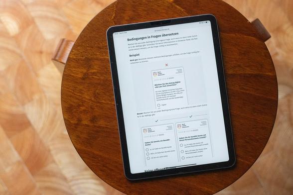A tabled computer on a walnut wooden stool showing a guide on good forms design with examples for ‘Translating conditions into questions’, illustrated by 3 simplified service interface