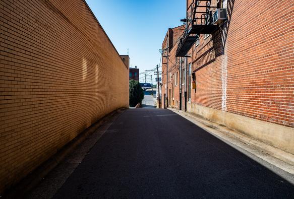 A narrow paved lane between two red brick industrial buildings and onward to a vanishing point in the distance.