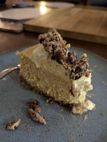 slice of butternut squash cheesecake on a dark green plate. the cheesecake has whipped cream and candied pecan topping.