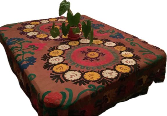 A colorful Uzbek Suzani tablecloth featuring intricate floral patterns in vibrant colors, with a small potted plant on top.