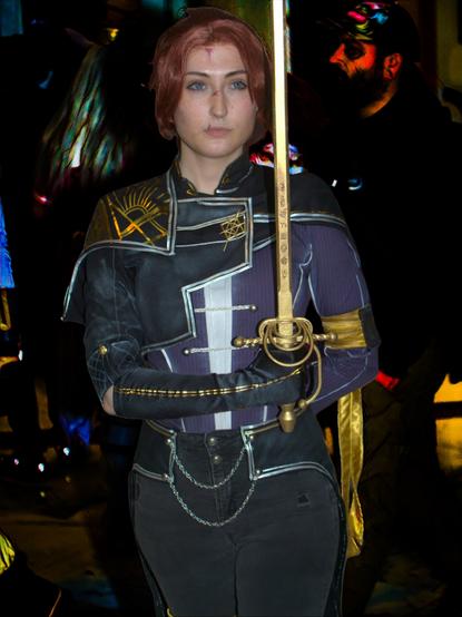 Threads user Gillianfoxglove cosplaying as Maelle from Expedition 33. The cosplayer is posing looking off to the side holding the sword up in her left hand, with her right hand off to her side