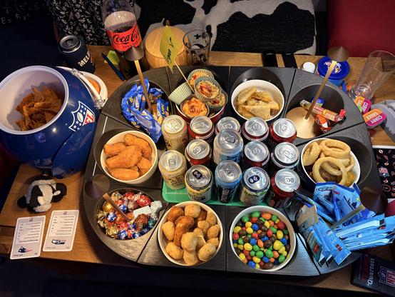 Top-Ansicht des mit einem Snackstadium und einem Snackhelm beinahe komplett gefüllten Couchtischs beim Superbowl-Gucken