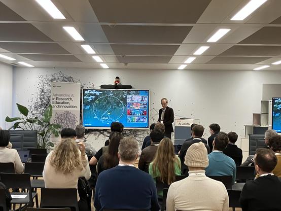 A speaker explains the Large Hadron Collider to people in a bright room