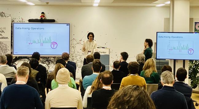 Two speakers presenting a slide on Data Mixing Operations with a colourful chart at a scientific meeting