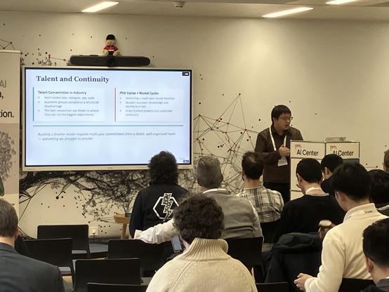 A speaker shares a slide on Talent and Continuity in front of an audience of tech leads of academic AI projects