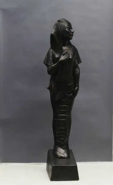 A woman wearing an ancient Egyptian headdress. She stands, one hand to her heart. The lower half of her body wrapped like a mummy. 

A quote from the artist: “Here was a group who had once made history and now after a long sleep was awaking, gradually unwinding the bandage of its mummied past and looking out on life again, expectant but unafraid and with at least a graceful gesture.”

For the exposition America’s Making ‘W. E. B. Du Bois, the noted writer, philosopher, and editor… commissioned sculptor Meta Vaux Warrick Fuller (1877–1968) to create an artwork that would symbolize the musical and industrial contributions of African Americans to the development of the United States. Fuller, who had studied both in Paris and at the Pennsylvania Museum School of the Industrial Arts, opted to take a different conceptual direction with her allegorical sculpture Ethiopia.’ ~ 
The National Museum of African American History and Culture