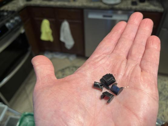A hand holding an assortment of small plastic bits that broke off the door of our microwave.