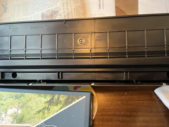 The lower portion of the outer door assembly from our microwave. There's a glass window at the top, and most of the photo is taken up by the panel's structural frame. It's a single, large piece of molded, black plastic, with a narrow channel at the very bottom. At approximately one quarter and three quarters of the photo's width, there are two bits of plastic that are dimly visible at the bottom of the channel, where the retaining clips from the previous photo broke off. The plastic was clearly too thin and brittle for the amount of stress the door goes through when it's opened.