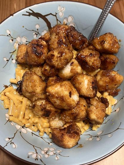 Photo of browned chicken cubes in a dark reddish sauce atop a bowl of Mac n cheese.