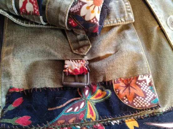 Gros plan sur une poche d'une veste en denim vert rapiécée avec un tissu coloré, on voit un papillon stylisé, à côté d'une feuille d'érable.
