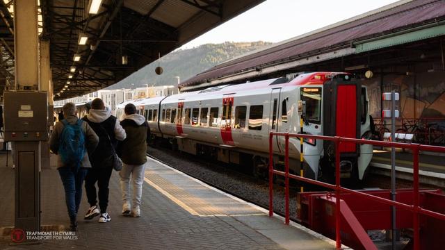 Modern Transport for Wales train stopped at Swansea Station platform with passengers walking nearby.