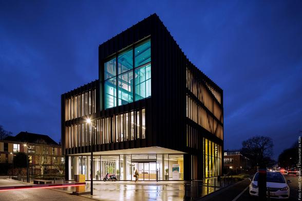 Modernes Gebäude bei Nacht mit großen Glasfenstern und blau beleuchtetem Innenraum.