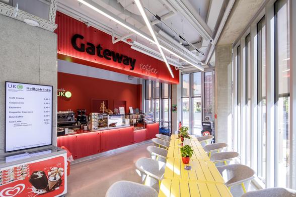 Kaffeebereich mit rotem Interieur, gelben Tischen und einem Menü mit Getränkepreisen an der Wand.