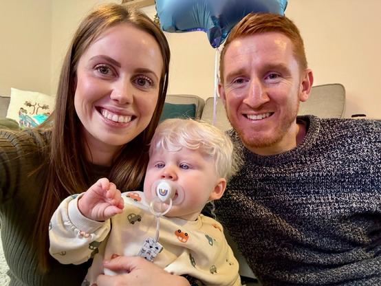 Mother, father and young child with albinism sitting together on a sofa, smiling at the camera.