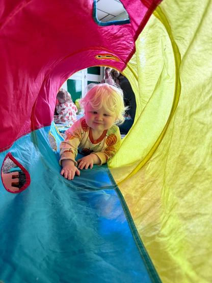 Young child with albinism crawling through a colourful play tunnel during a sensory play session.