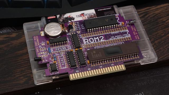 A MouseBiteLabs PCB with EPROM, SRAM, and other components soldered to it.  The PCB is pinkish purple and sitting on top of the front of a custom FF6 shell.