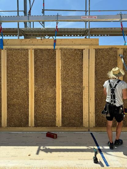 Guy with sun hat working on assembly of prefabricated straw panels